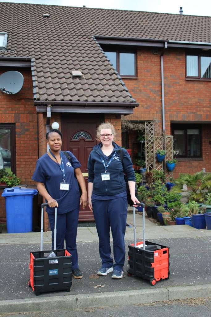 Two female nurses standing outside a house with research equipment